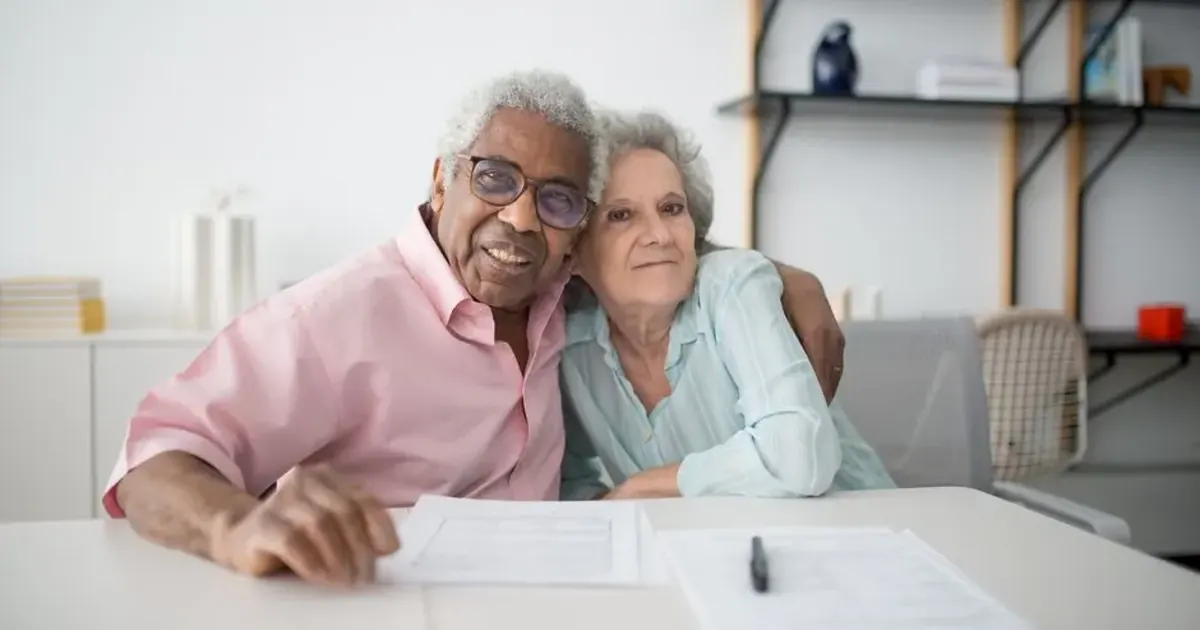 Couple de seniors souriants qui consultent des documents à table
